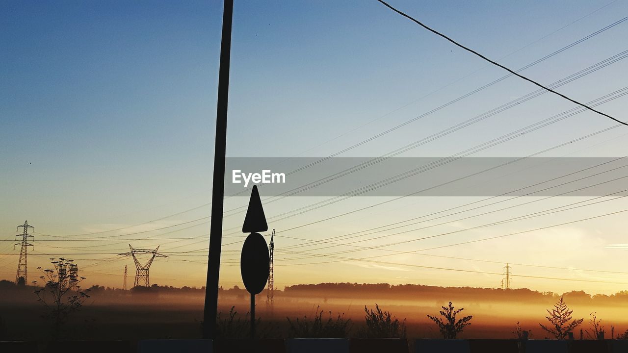 Power line above landscape in foggy weather during sunrise