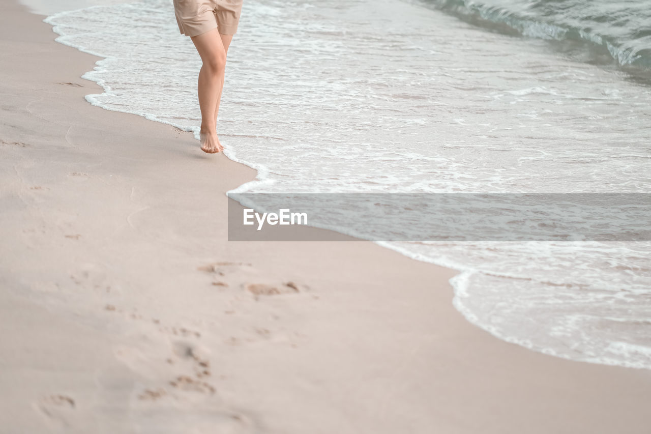 beach, land, sand, water, sea, one person, holiday, vacation, trip, barefoot, low section, white, adult, nature, leisure activity, motion, walking, human leg, women, day, lifestyles, limb, human limb, surfing, wave, standing, sports, shore, outdoors, travel, summer, water sports, relaxation, human foot, travel destinations, tranquility, water's edge, beauty in nature, rear view, enjoyment, footprint, copy space, clothing, dress, shoe, young adult, female, carefree