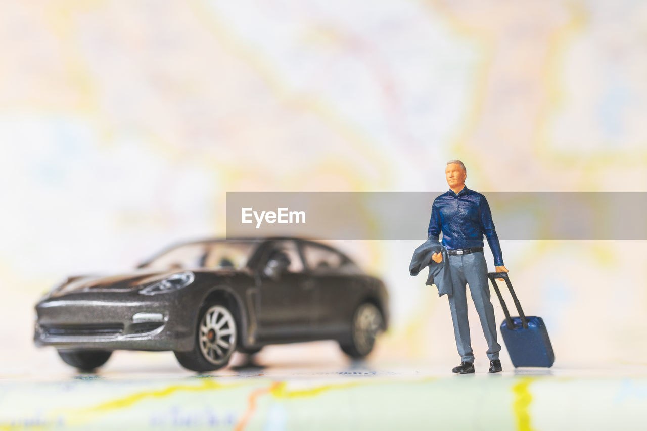 car, mode of transportation, transportation, toy, motor vehicle, men, business, adult, cartoon, full length, one person, vehicle, automobile, businessman, travel, copy space, land vehicle, driving, childhood, day, indoors, occupation, selective focus, business travel, standing, yellow, suitcase