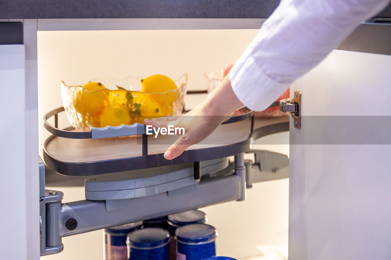 Hand pushes modern pull-out shelf with lemons  in kitchen cupboard 