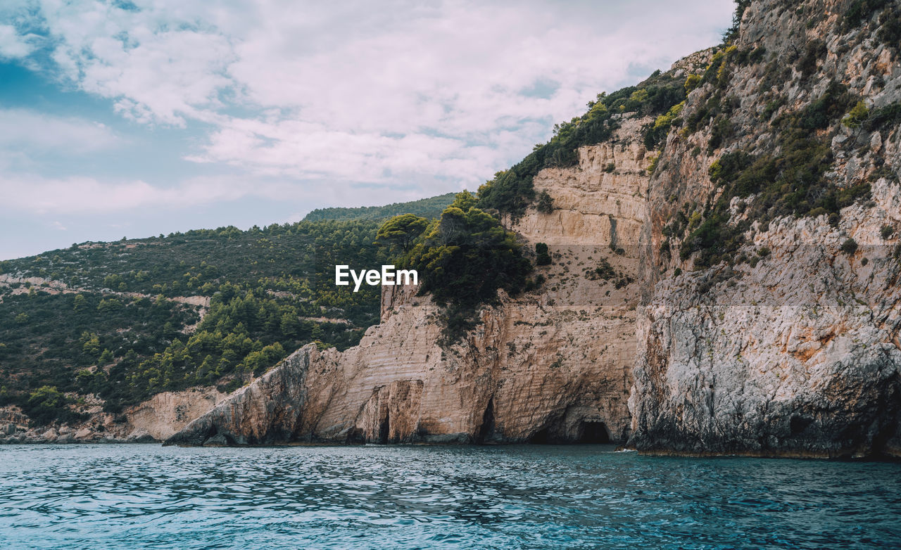 Scenic view of sea by mountain against sky