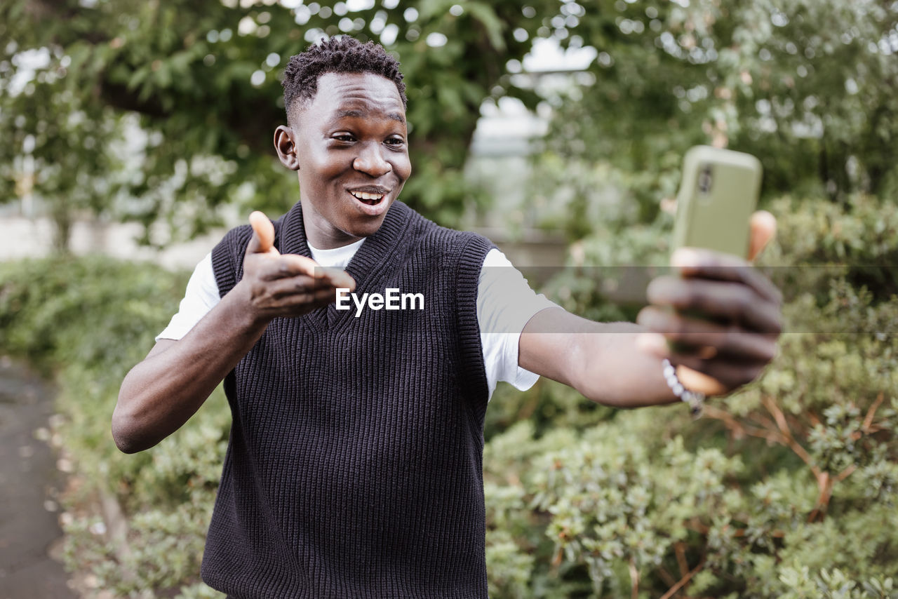 Young african man taking selfie or vlogging on phone in park, smiling