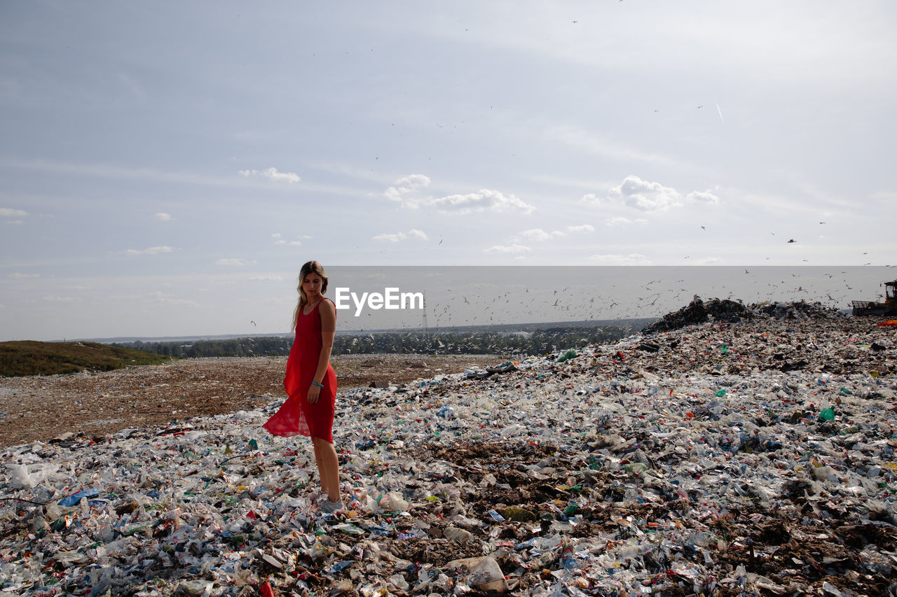 Young woman standing on garbage against sky