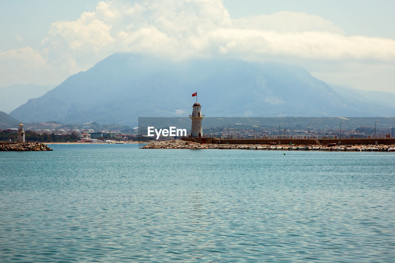 Lighthouse amidst buildings and mountains against sky