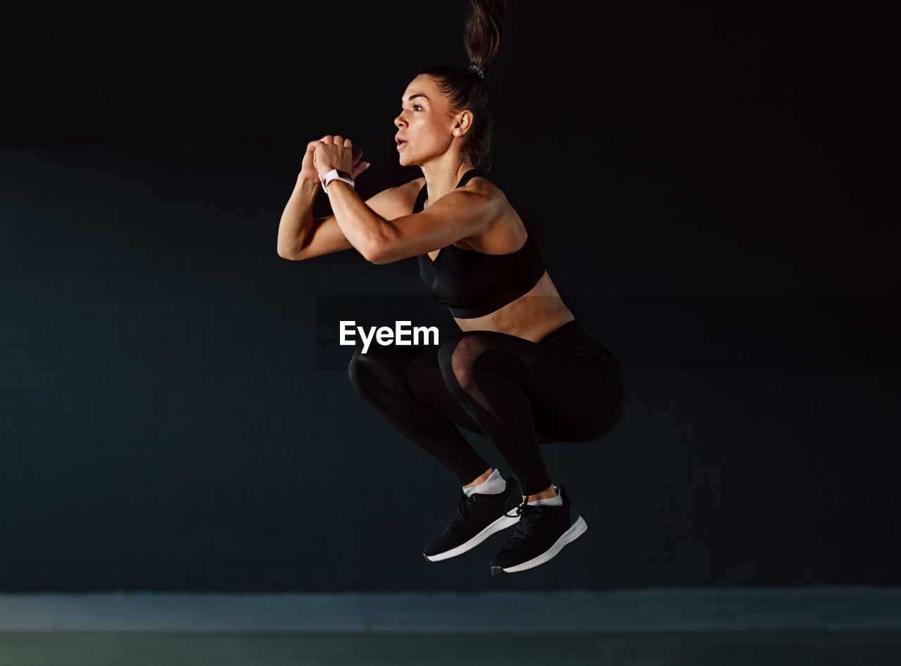 Full length of woman exercising against black background