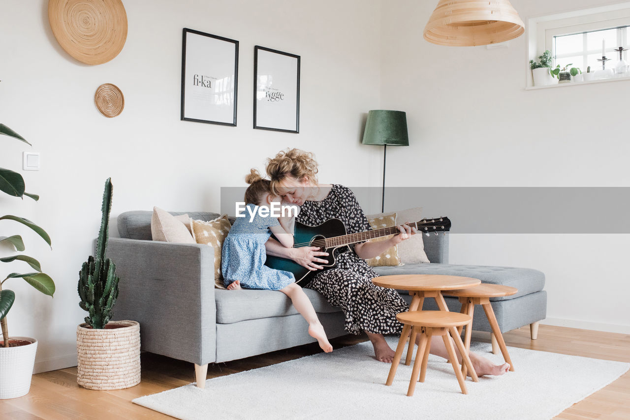 Mother and daughter cuddling whilst playing the guitar at home