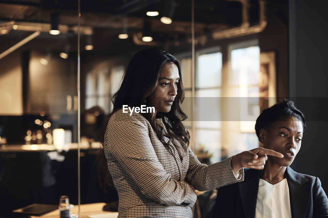 Businesswoman pointing while talking to female colleague at office