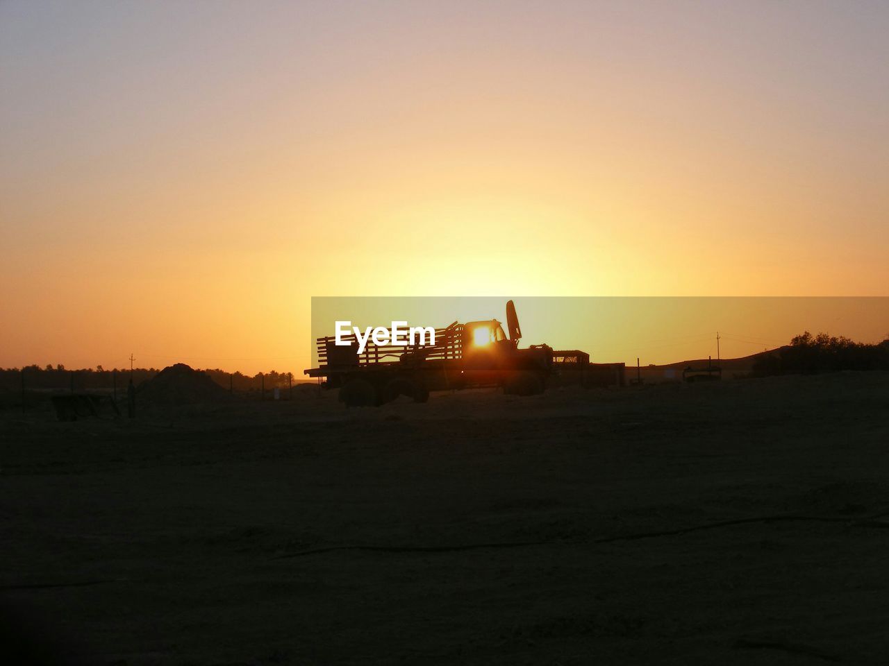 Truck on field against clear sky at sunset