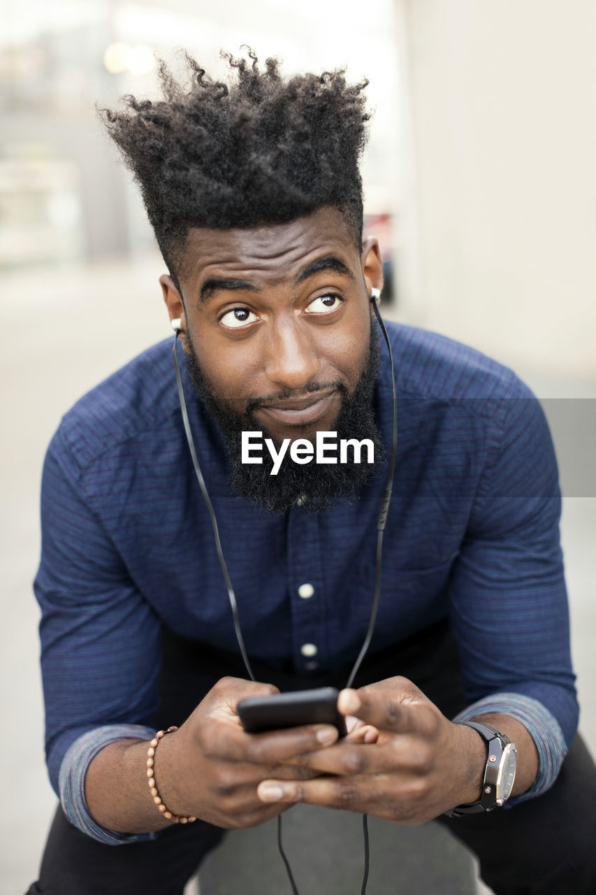 Man listening to music from mobile phone while looking away in city