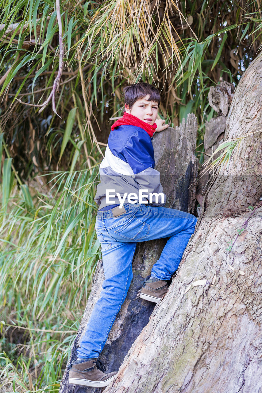 Portrait of teenage boy climbing on rock in forest