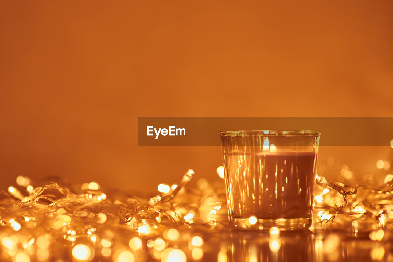 Burning candle with golden garland lights in bokeh on dark background