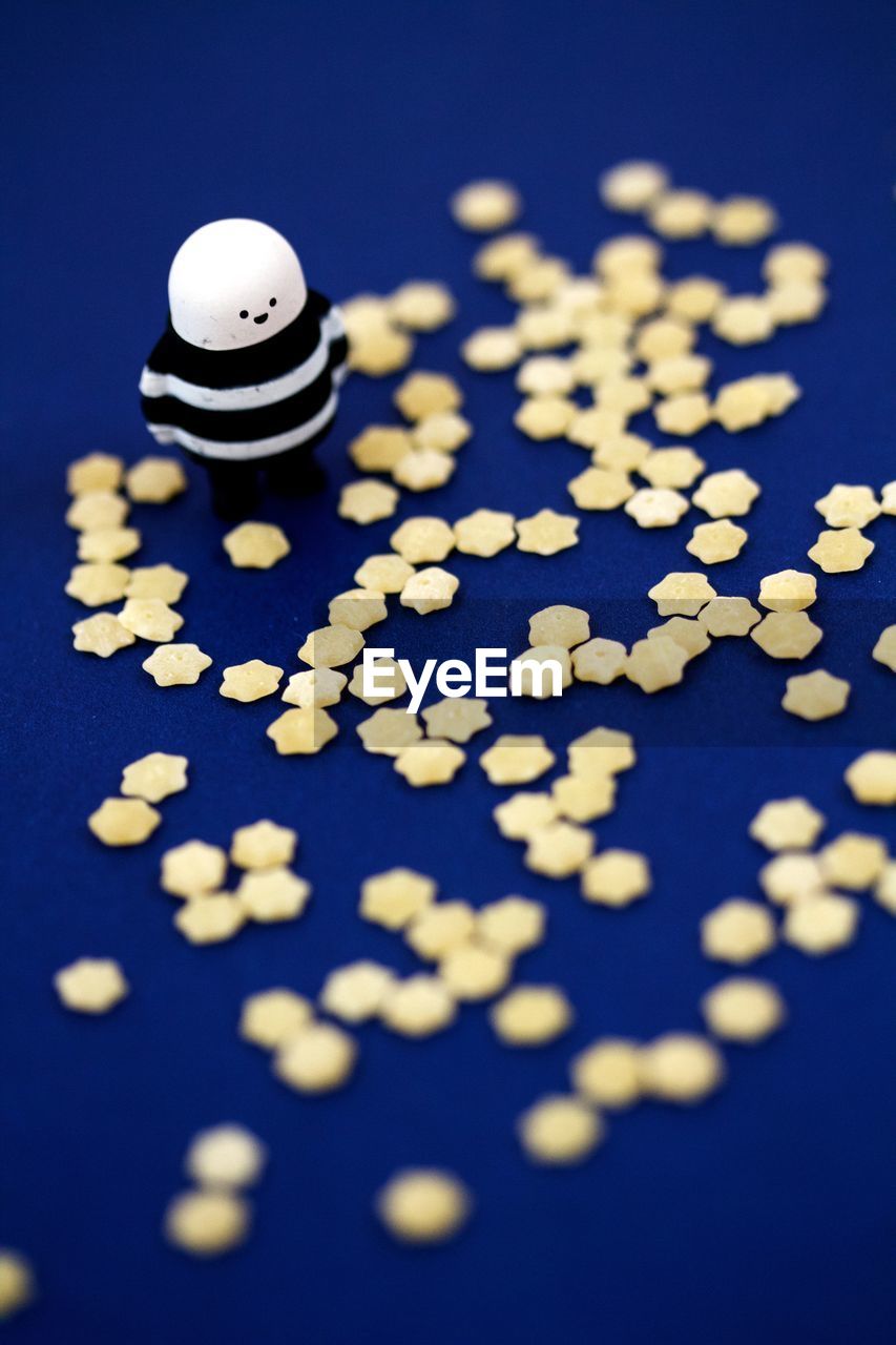 High angle view of stelline pasta with figurine on blue table