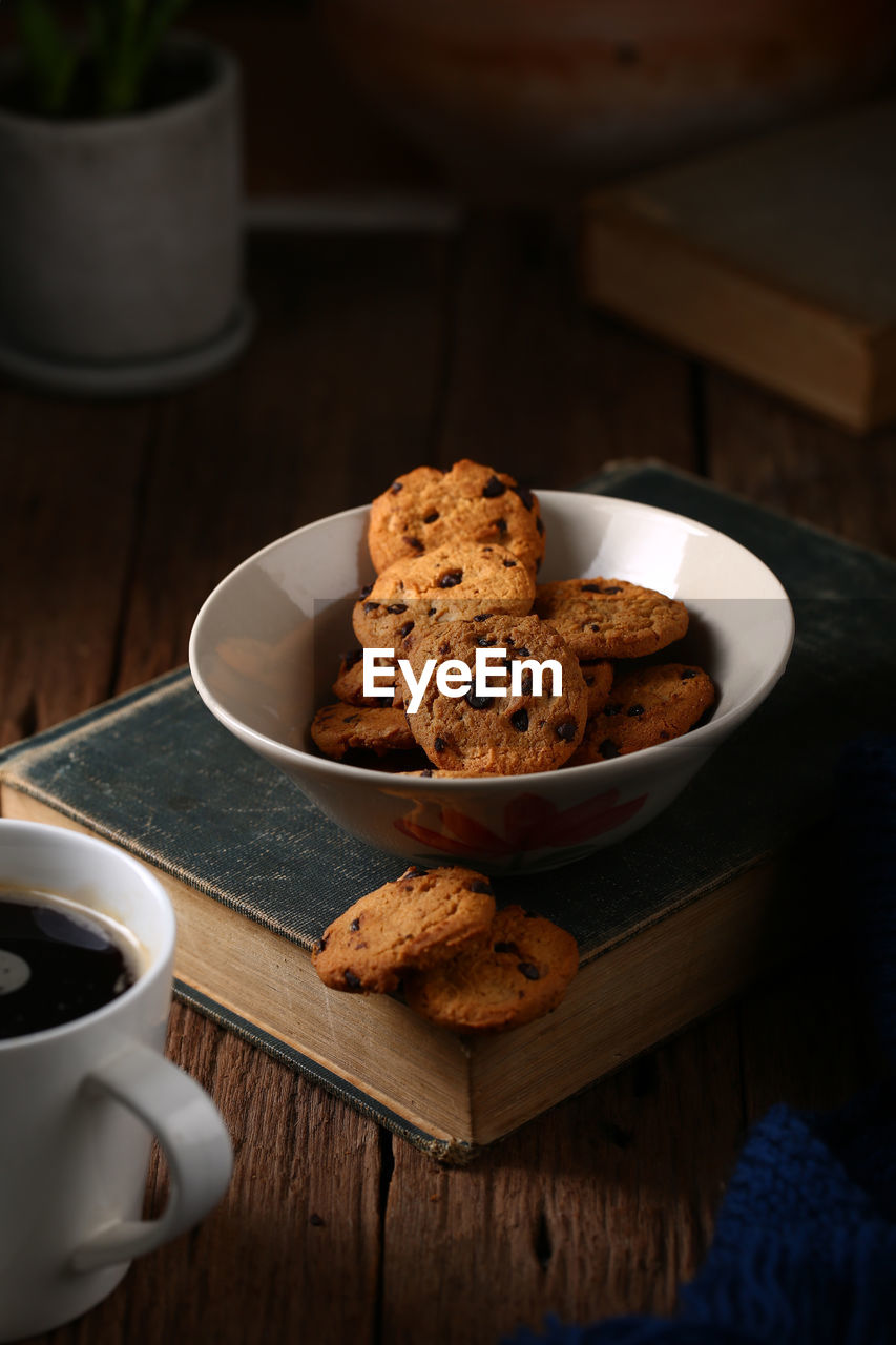 Still life with chocolate chip cookies in cup bowl on old book