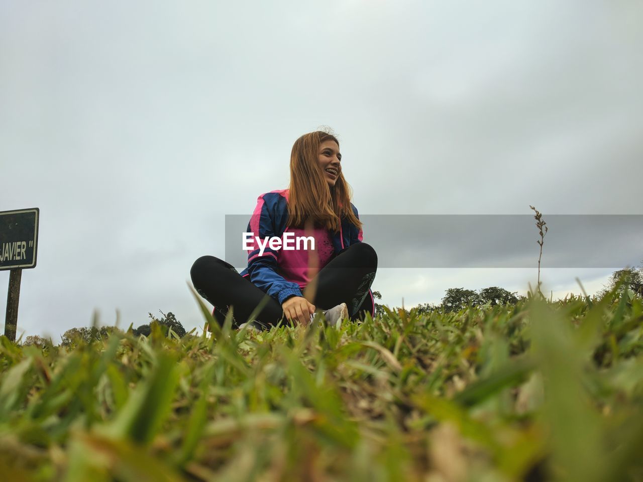 Low angle view of young woman sitting on grass against sky