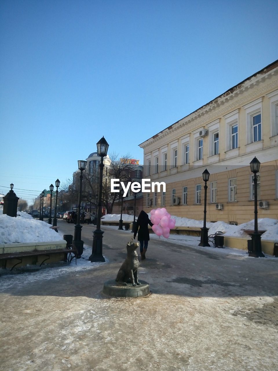 Statue behind woman walking with balloons on street during winter