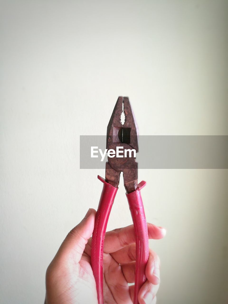 Close-up of hand holding pliers against white background