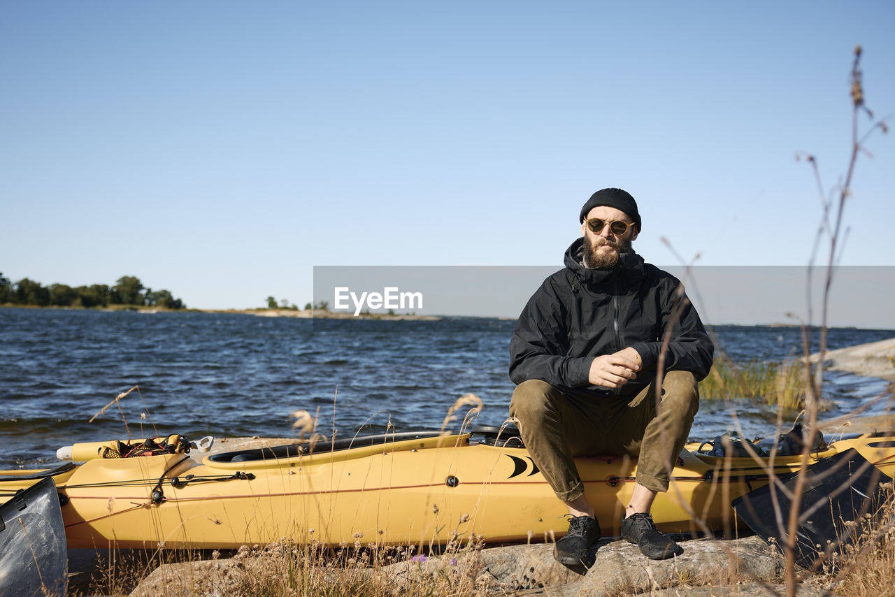 Man sitting on kayak on coast and looking at camera