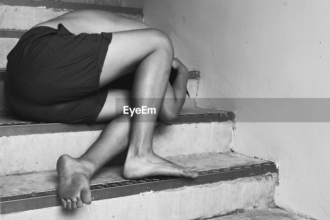 LOW SECTION OF WOMAN SITTING ON STEPS AGAINST WALL