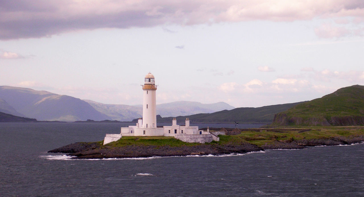 Lighthouse on hill against cloudy sky