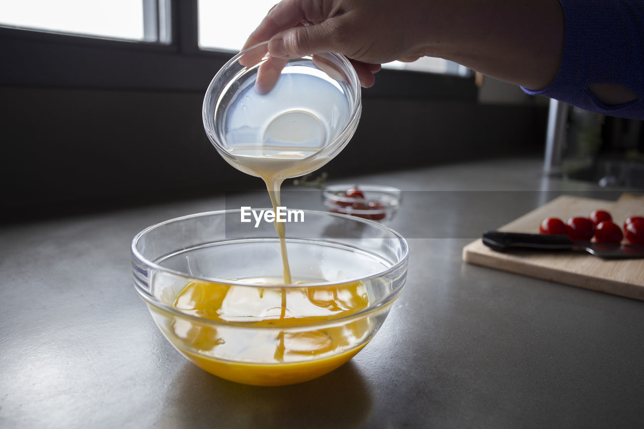 Pouring milk into egg batter, sliced tomatoes in background.