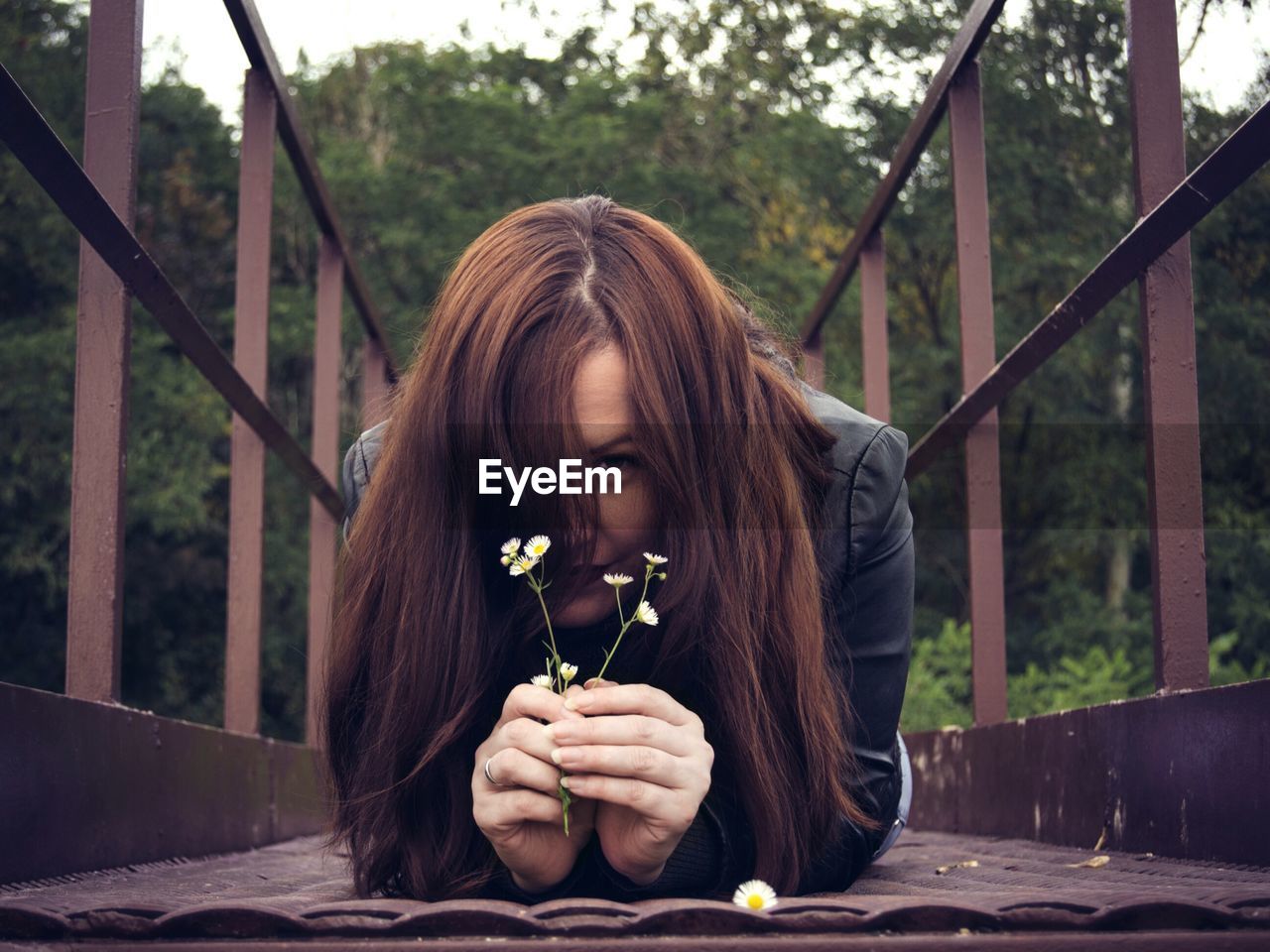 Portrait of young woman holding flower while lying on footbridge