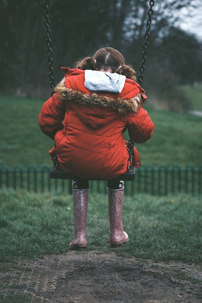 Rear view of girl wearing warm clothing sitting on swing