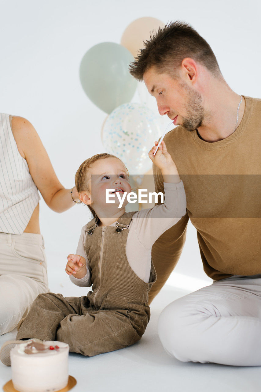 men, two people, adult, parent, indoors, family, toddler, childhood, child, father, baby, togetherness, person, emotion, sitting, lifestyles, one parent, women, domestic life, female, positive emotion, bonding, domestic room, home interior, holding, food and drink, happiness, love, looking, furniture, casual clothing, fun, food, smiling, care, tableware