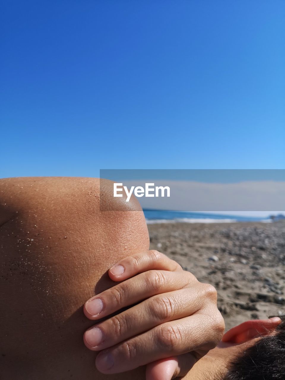 Close-up of man lying down at beach against blue sky