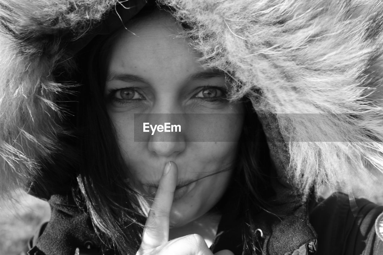 Close-up portrait of woman wearing warm clothing with finger on lips