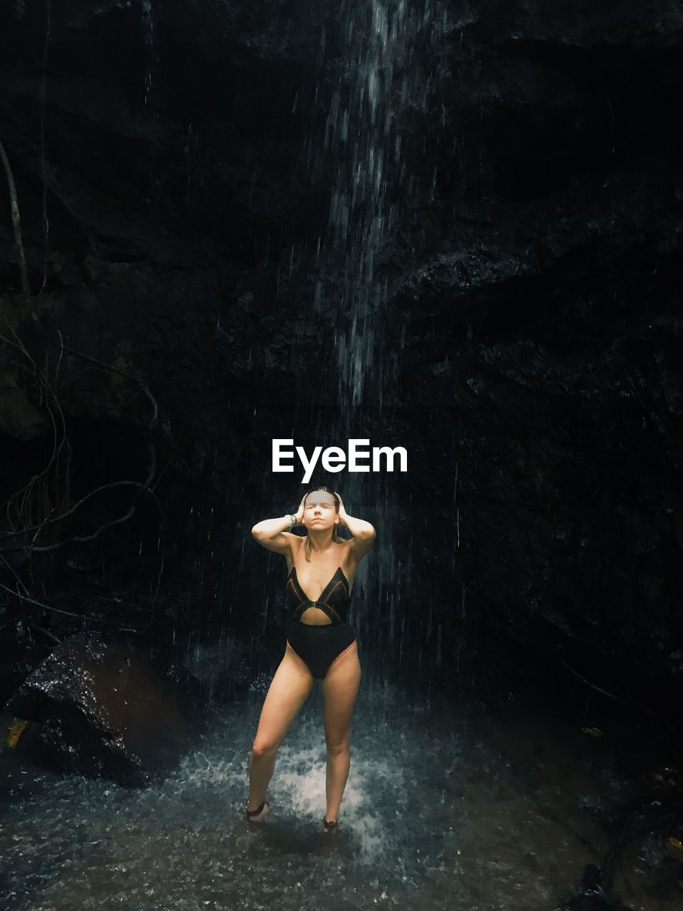Young woman in bikini standing under waterfall in forest