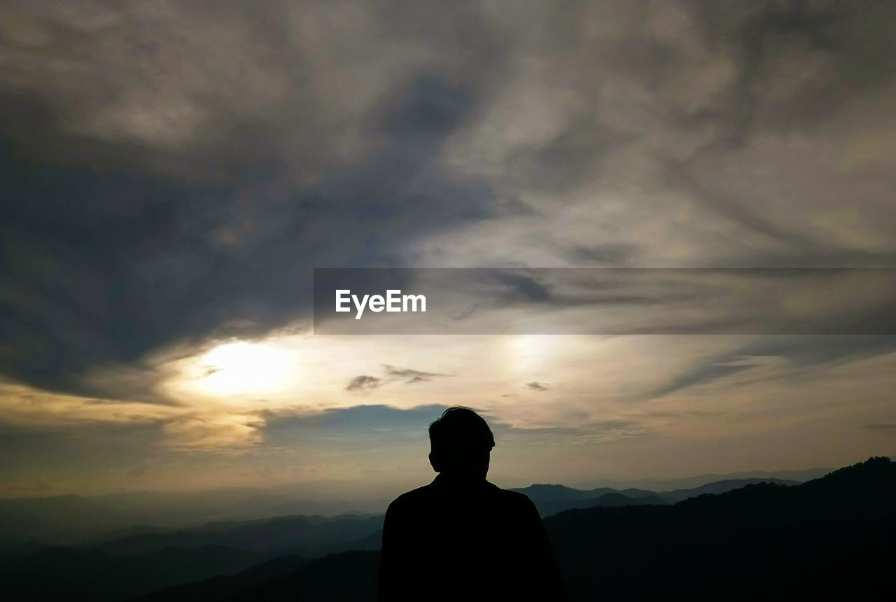 REAR VIEW OF SILHOUETTE MAN STANDING AGAINST SKY AT SUNSET