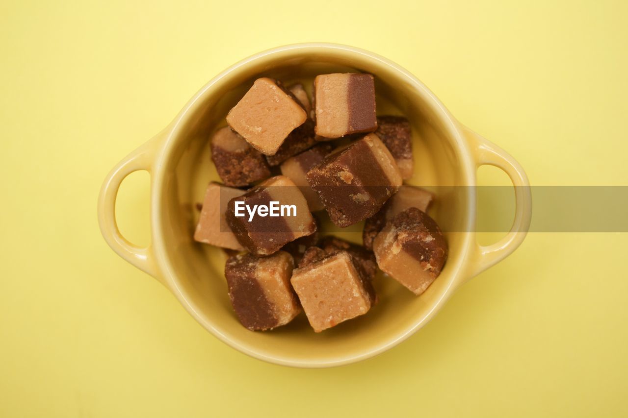 High angle view of sugar cube in bowl over yellow background