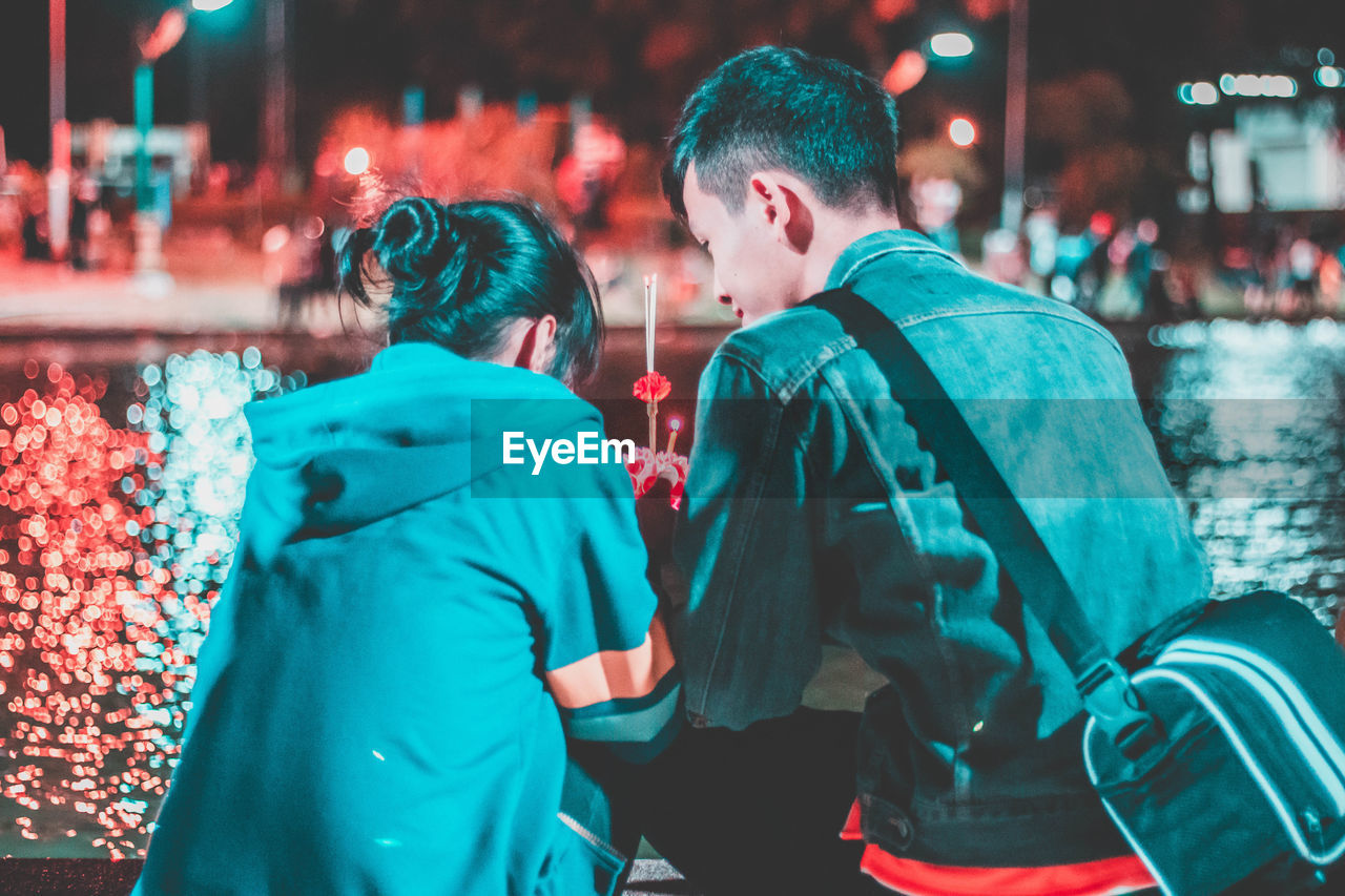 Rear view of couple sitting in city at night