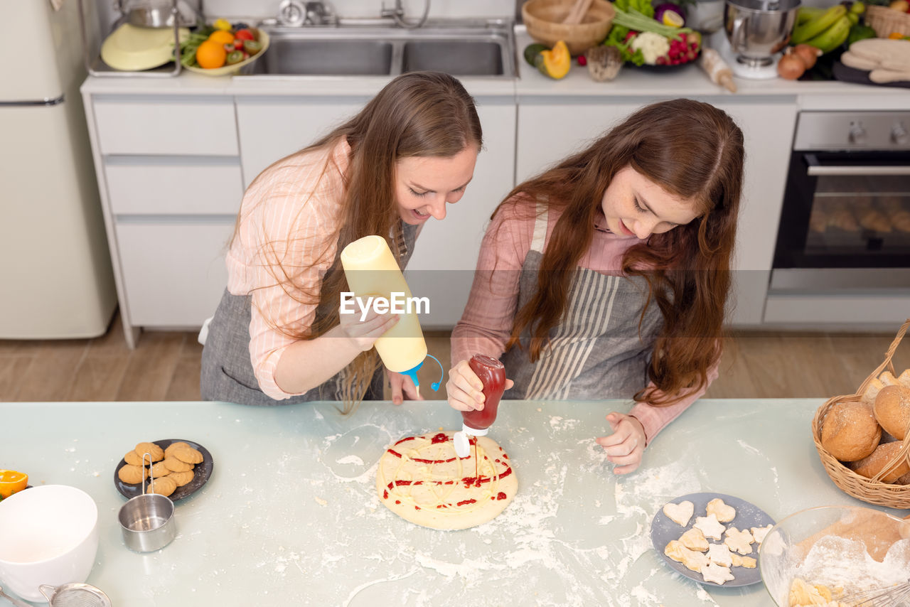 In the kitchen at home, a playful mother and daughter yell while making pizza dough.