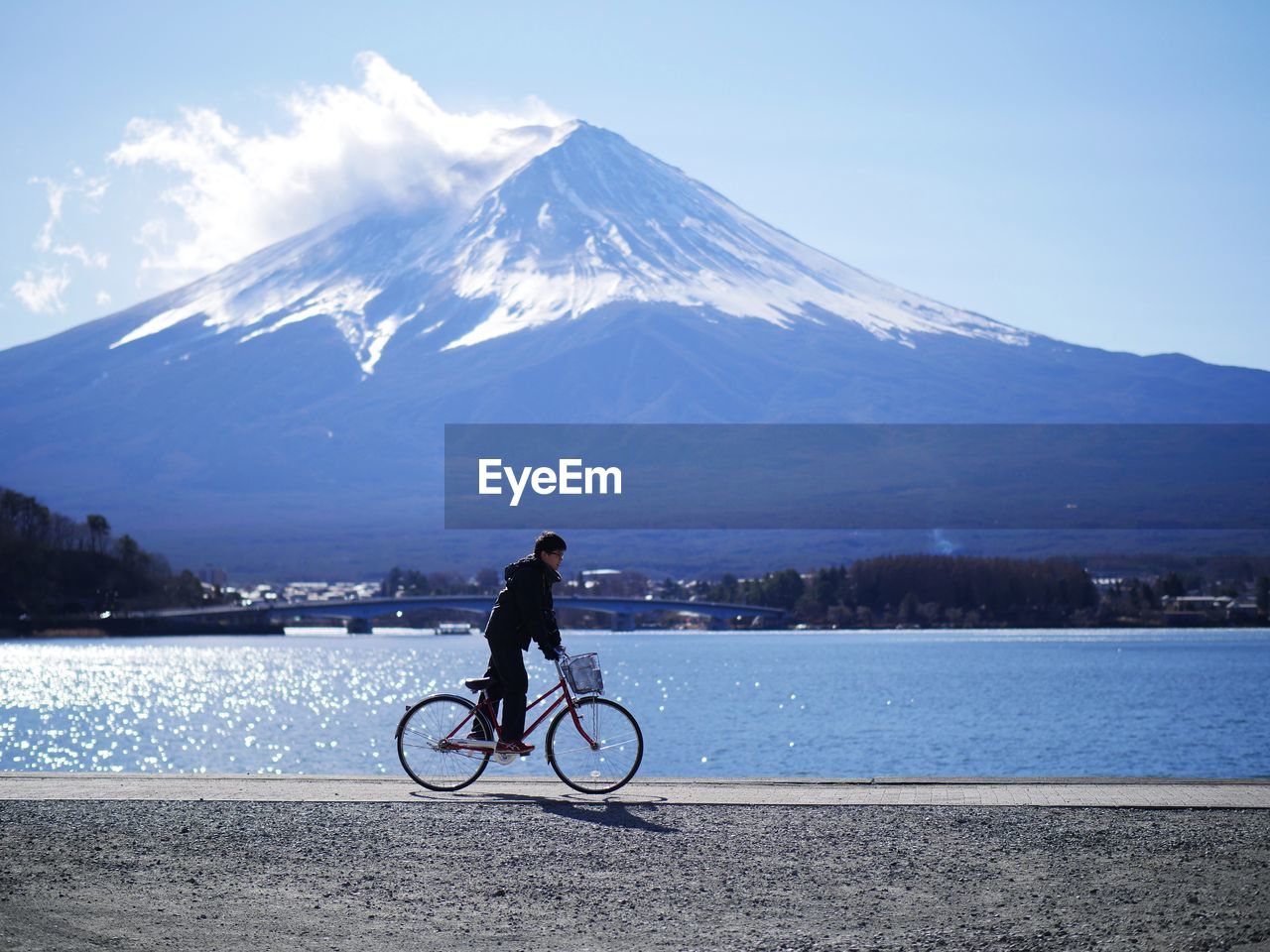 Man riding bicycle by river against mountain and sky