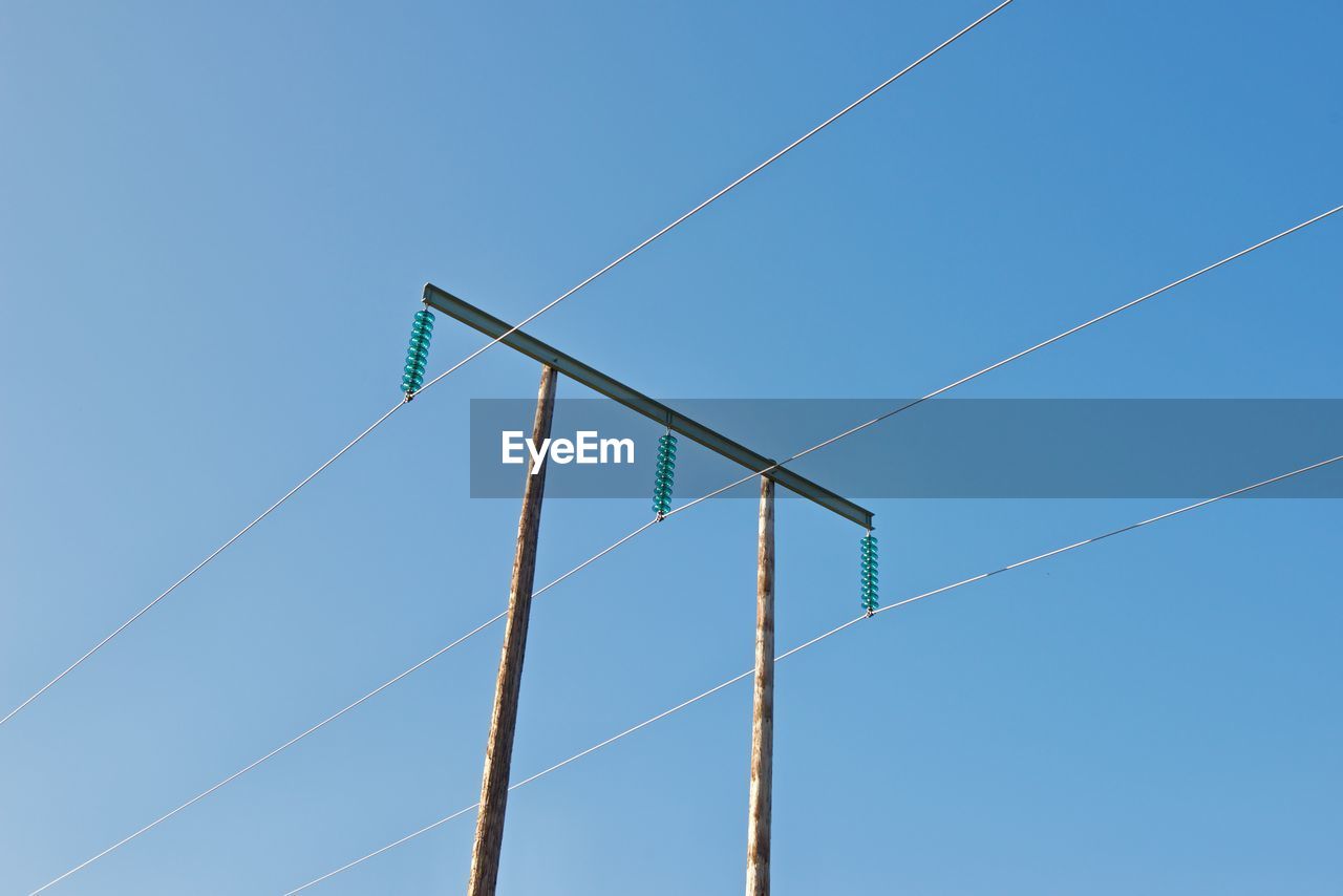 Low angle view of telephone pole against clear blue sky