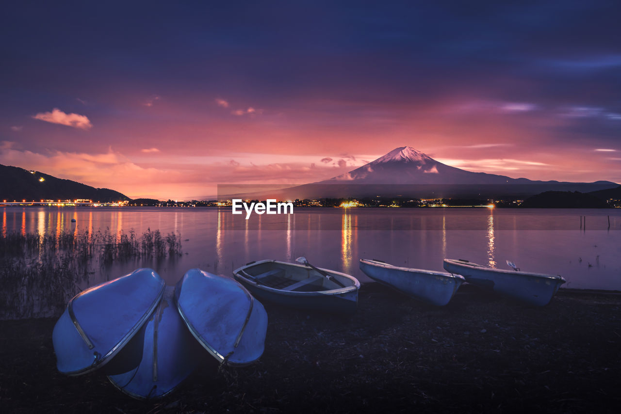 Boats moored on lake against sky during sunset