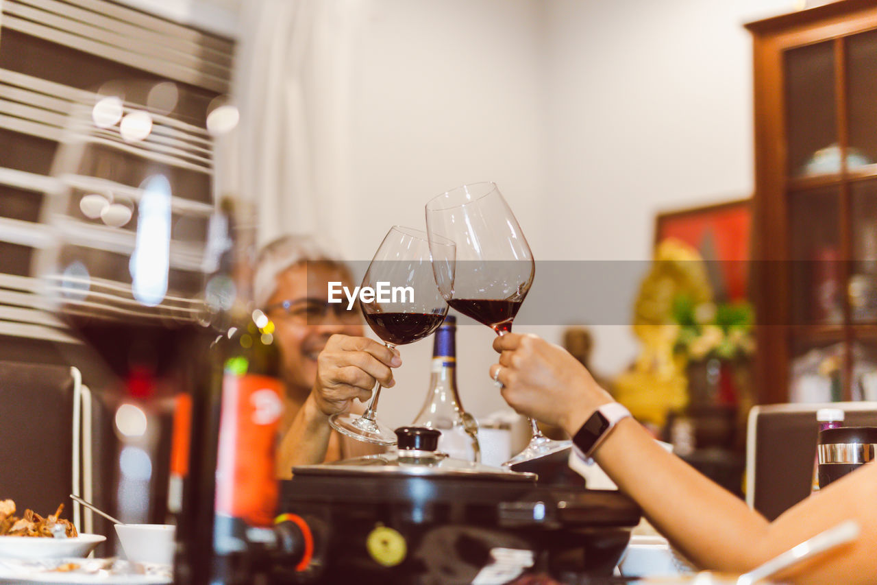 Couple making toast with glasses of red at dinner.