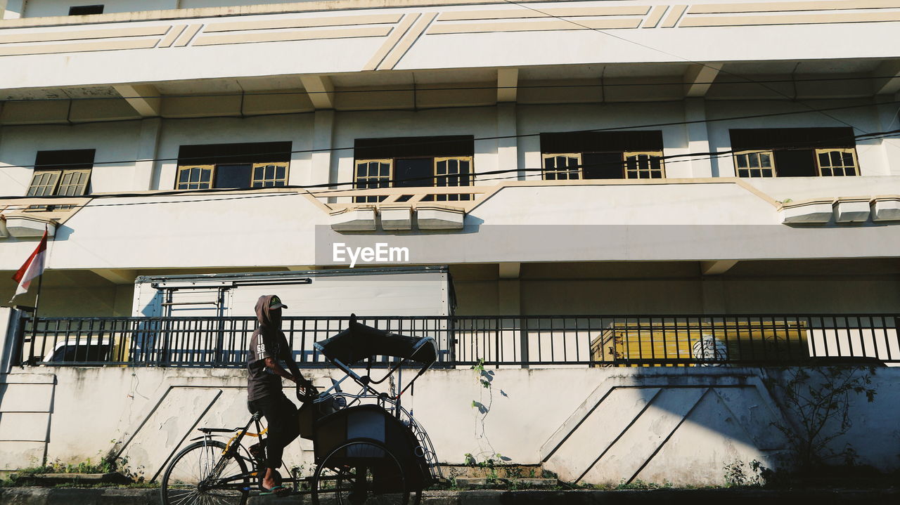 FULL LENGTH OF MAN WITH BICYCLE ON BUILDING