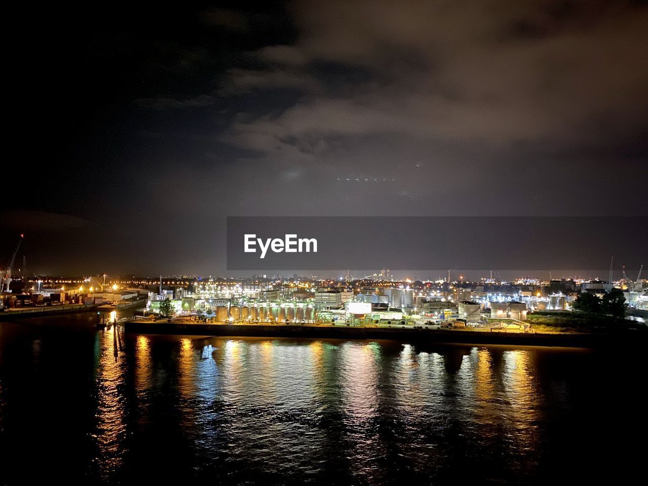 Illuminated buildings by river against sky at night