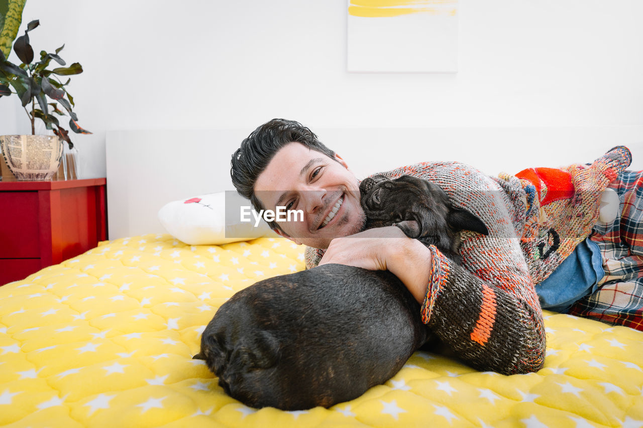 Portrait of smiling young man playing with dog on bed at home