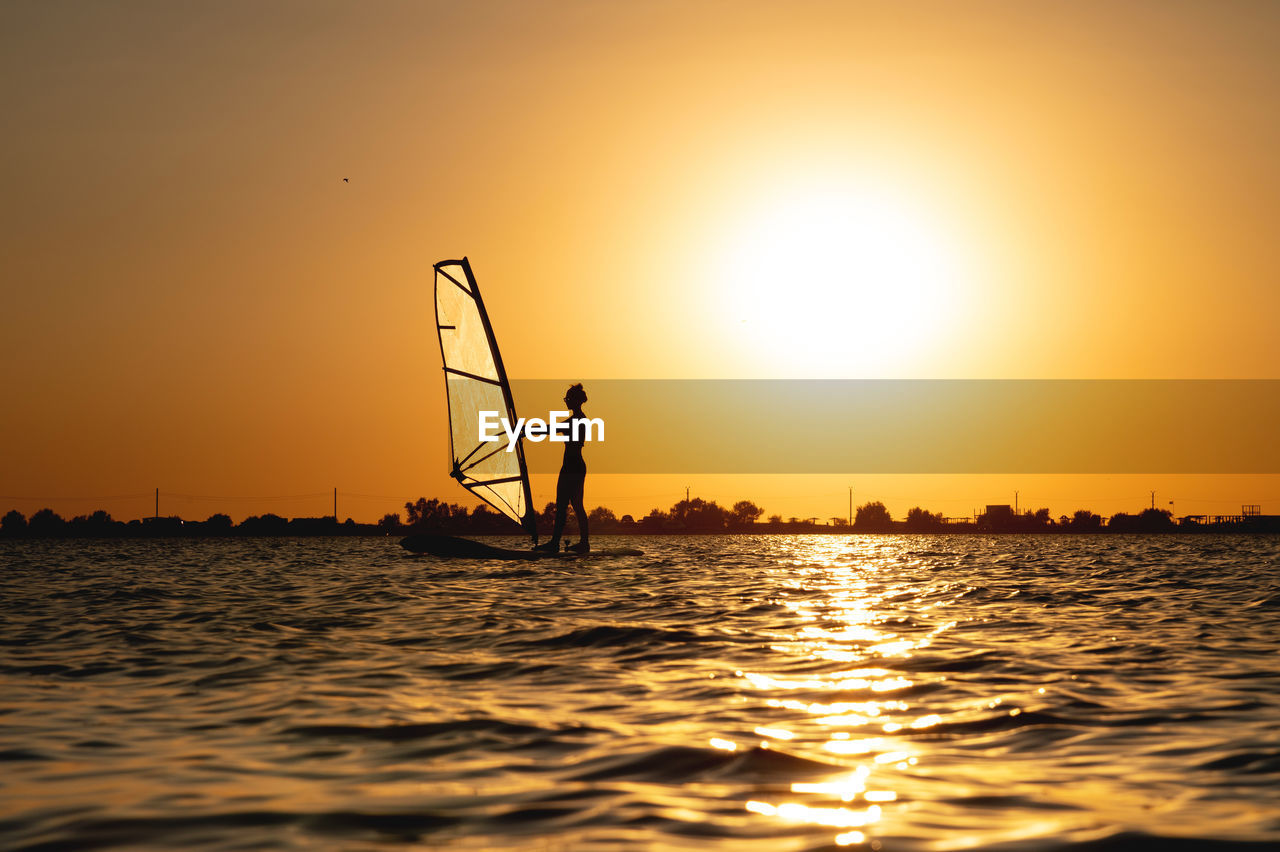 Woman windsurfer silhouette at lake sunset. beautiful beach landscape. summer water sports 