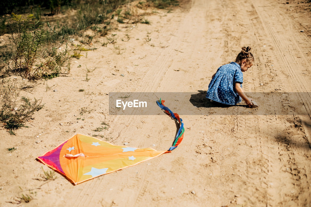 Rear view of a baby in a blue dress and a kite lying on a sandy road