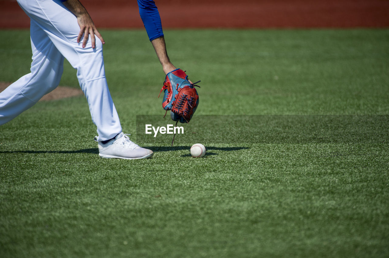 Low section of player picking baseball on grass