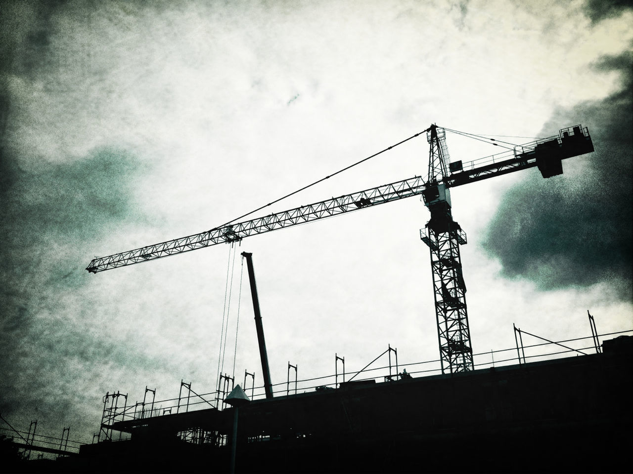 LOW ANGLE VIEW OF CRANES AT CONSTRUCTION SITE AGAINST CLOUDY SKY