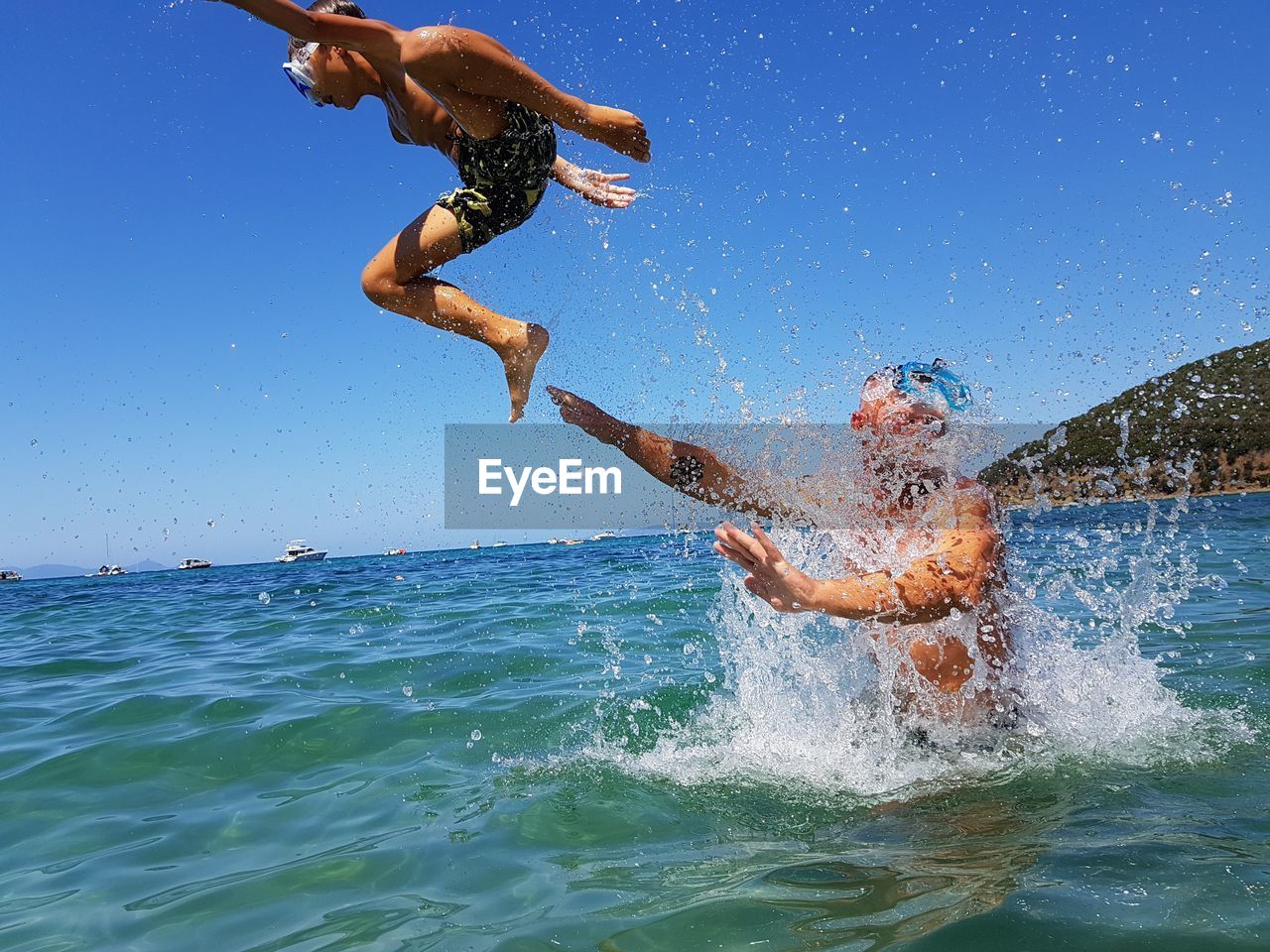 Playful father throwing son in sea against clear sky