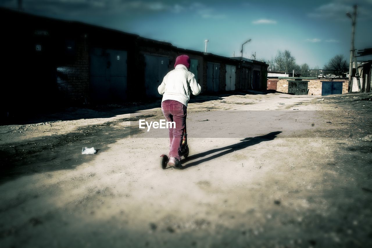 Full length rear view of boy riding scooter on street