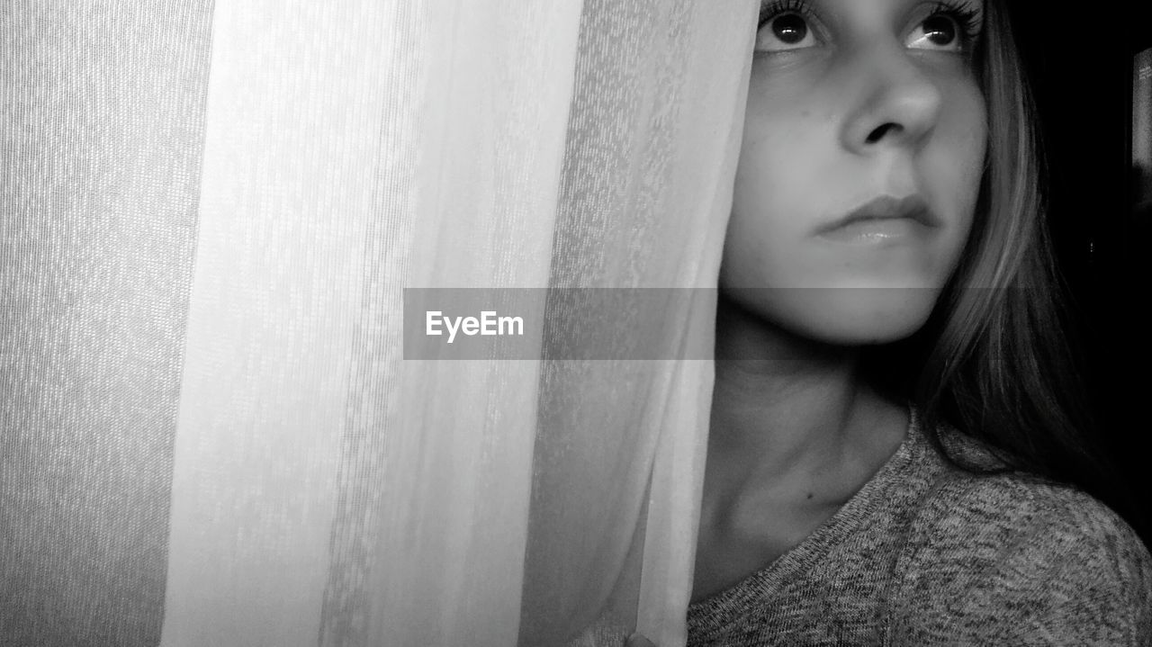 Close-up of thoughtful girl standing by curtain