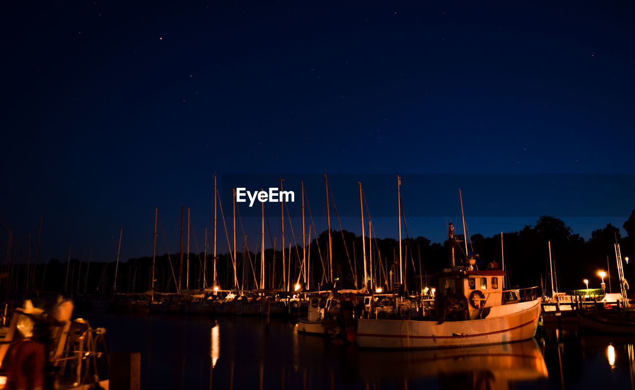 Boats moored at harbor against clear sky at night