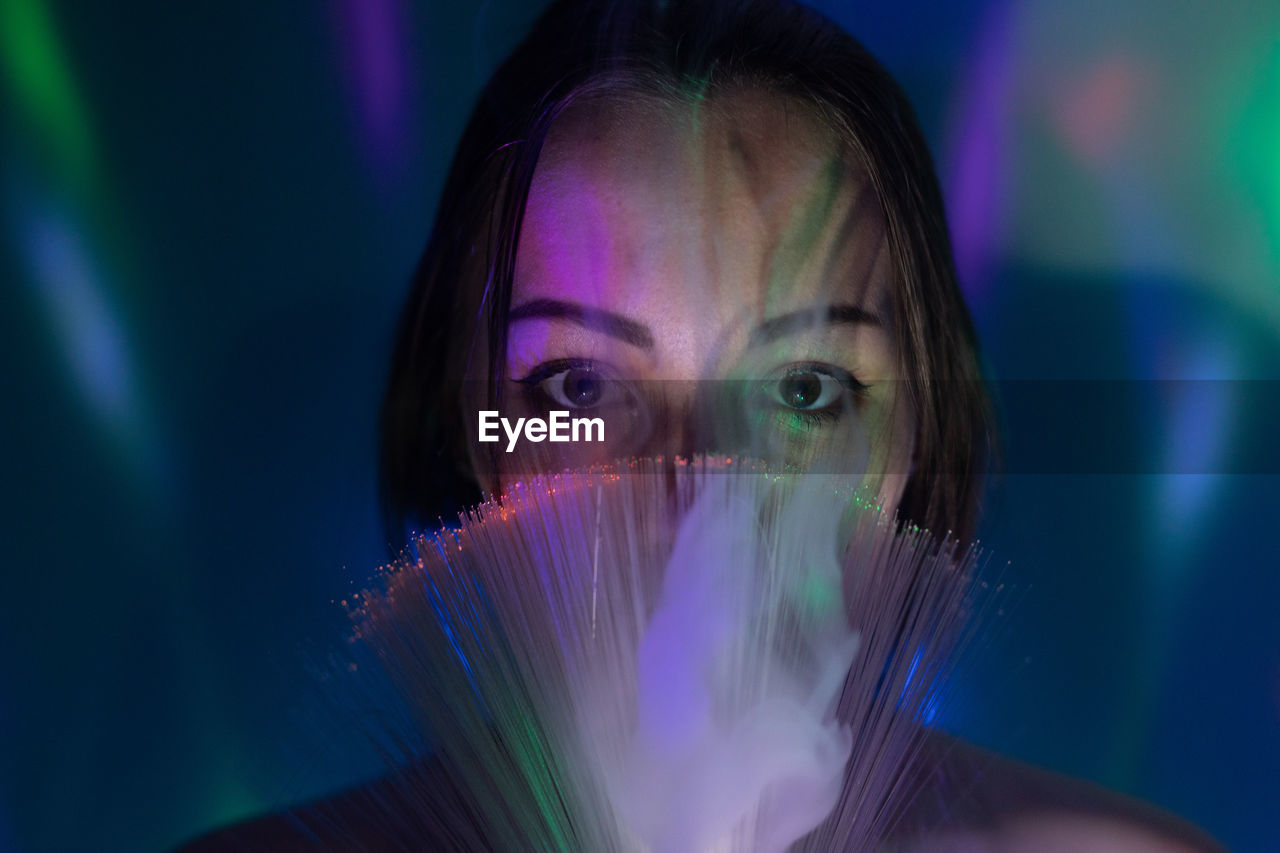 Close-up portrait of young woman holding multi colored fiber optic